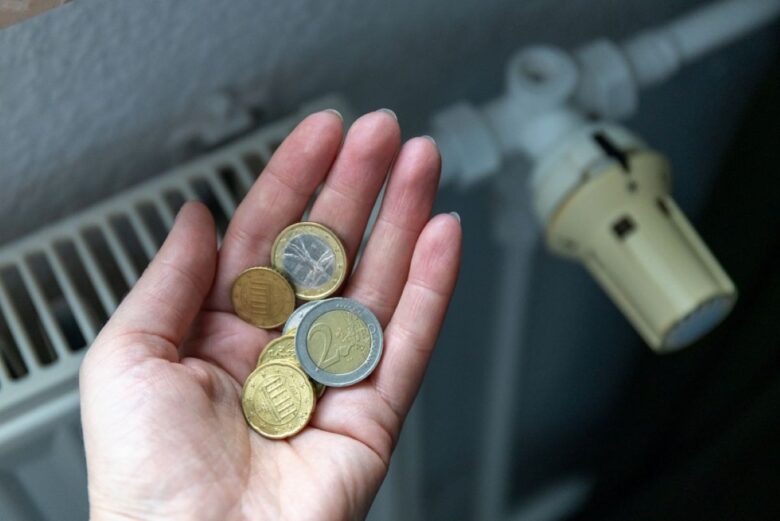 Mano con delle monete davanti a un termosifone